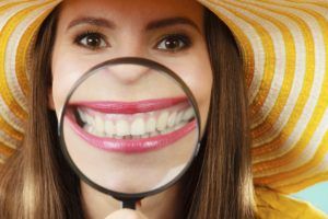 Closeup funny woman in summer hat smiling and show teeth through a magnifying glass